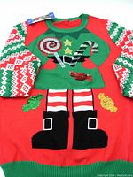 Red and green Santa's Elf Christmas sweater laid flat showing candy and elf boot designs on front.