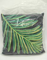 Navy blue 16-inch square cushion with a large green and yellow leaf embroidery, shown sealed in clear plastic packaging from front and back views.
