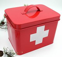 Front view of red metal first aid kit tin box with white cross symbol and handle on top.