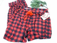 Red and black buffalo plaid lounge pants laid out flat, showing fabric pattern and pom-pom drawstring detail.