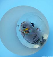 Side angle showing frosted circular base with clear dome featuring carved Maltese cross and colorful internal element resembling an egg.