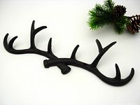 Black cast iron rack shaped like crossed antlers with detailed antler prongs shown angled for display with pine and pinecones.
