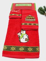 Full view of three red towels with snowman embroidery and green-gold decorative trim, showing large bath towel, hand towel, and washcloth