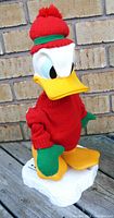 Front view of vintage 1997 Donald Duck skating figurine showing red sweater, knit red hat with pompom, green mittens, yellow beak and feet, standing on white skating base.