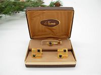Open di Gino box with gold tone tie bar and pair of cuff links exhibiting geometric design and dark square stones.