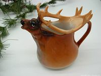 Side profile of a ceramic creamer shaped like an elk, showing the detailed antlers and brown gradient color.