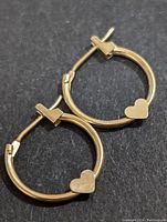 Two 10K gold hoop earrings placed on black surface showing heart shape charm detail and hinged clasp.