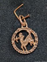 Front view of 10K gold pendant depicting ram motif, hanging from a pin on black cloth.