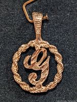 Close-up image of the front of a 10K gold pendant shaped like the letter G within a circular twisted rope border.