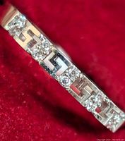 Close-up image of ring's front showing 10K gold band with alternating Greek key pattern design and sparkling cubic zirconia stones on a red velvet background.