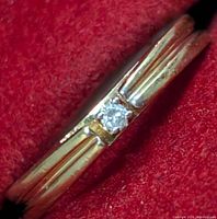 Close-up view of the diamond set in the 10K gold band showing its bezeled square mounting and the textured yellow gold on either side.