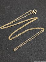 Image showing the full length of the thin gold chain laid out on a black background, clearly displaying the fine link style and the spring ring clasp.