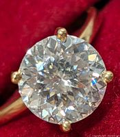 Close-up of ring top showing round moissanite and six-prong setting against red background