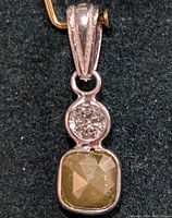 Front view of pendant showing round brilliant diamond above cushion cut fancy brownish yellow diamond