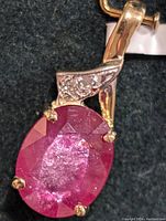 Close-up of the certified 14K gold pendant with an oval-shaped, faceted deep pink glass-filled ruby and a small diamond accent near the bail.