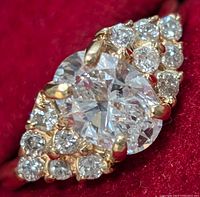 Close-up of ring front showing oval lab-grown center diamond and surrounding natural diamonds on red background