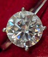 Close-up on round brilliant-cut moissanite showing facets and clarity against red background.