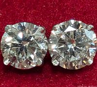 Two round brilliant cut diamonds in four-prong white gold settings on red background
