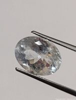 Close-up photo of an oval light blue aquamarine gemstone held by tweezers.