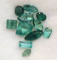 Close-up image of 11 loose genuine emerald stones in various shapes and cuts on a white background