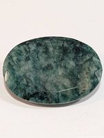 Top view of oval cut emerald gemstone showing deep and light green inclusions and faceted surface