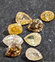 Eight loose fancy color diamonds arranged on dark surface, showing assorted shapes and colors