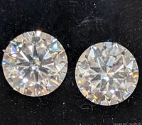 Close-up of two clear, round cut moissanite gemstones on black background showing facets and brilliance.