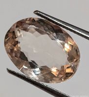 Oval faceted morganite gemstone with light peach-pink hue, held by tweezers