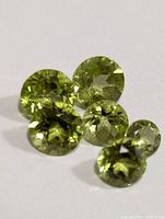Close-up of 5 loose round faceted green peridot gemstones placed on white background showing color and facets.
