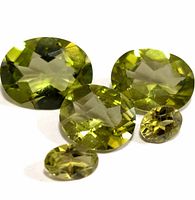 Four oval faceted green peridot gemstones shown on white and black backgrounds to highlight color and facets.