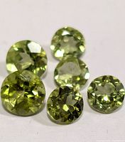 Close-up photo of six round faceted light green peridot gemstones on a white surface, showing clarity and cut details.