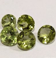 Close-up image of all five round faceted light green peridot gemstones laid on a white surface. Shows clarity and cut details.