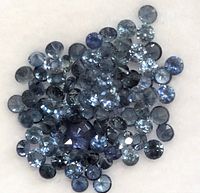 Close-up of multiple small round blue sapphire gemstones loosely grouped on a white background.