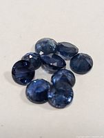 Close-up photo showing nine loose faceted blue sapphires on a white background, showcasing their deep blue color and faceting.