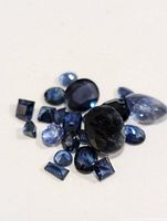Collection of loose genuine sapphire gemstones of varying shapes and sizes viewed from above on a plain surface.