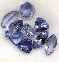 Eight loose faceted tanzanite stones arranged on neutral background, showing color and cuts
