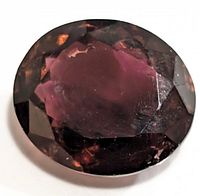 Close-up image of a deep reddish-brown oval faceted tourmaline gemstone highlighting the facets and color.