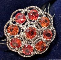Close-up view of the silver ring showing the cluster of round orange sapphire appearance stones securely prong-set in silver metal, highlighting the colors and sparkle of the stones.