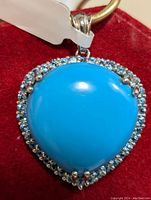 Close-up image showcasing the bright blue teardrop turquoise pendant framed with small blue topaz stones on a cord.