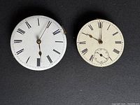 Two vintage pocket watch movements with white enamel dials and key wind fusee mechanical movements shown from front with visible Roman numerals and aged watch hands.