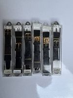 Photo showing six individual black leather watch straps with lizard texture in clear retail boxes labeled Cardinal and Leather Cuir, tagged size 18mm and $8.95 retail price.