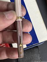 Close-up image of vintage Conway Stewart Dinkie fountain pen held in hand showing pink marbled body, gold clip with emblem, and gold band.