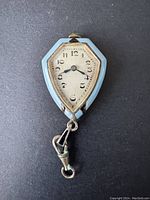 Front view of vintage pendant watch showing dial with Arabic numerals and black hands surrounded by light blue enamel