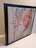 Side angle showing thickness and black frame of framed Spider-Man wall art on wooden panels.