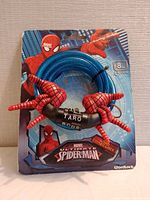 Front view of Marvel Ultimate Spider-Man bike lock with red spider hand grips, blue cable coiled, combination lock with code visible, sealed in original branded packaging.