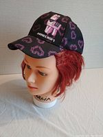 Black baseball cap on mannequin head showing front design with embroidered Minecraft logo and pink Creeper pixel designs.