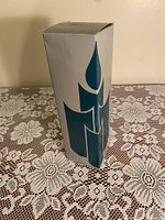 White and blue box with candle graphics on tablecloth lace background. Minor storage wear visible on box.