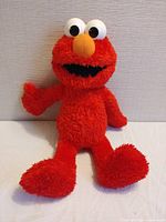 Full view of the red Elmo plush toy sitting against a wall.