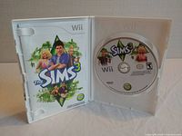 Open Nintendo Wii case showing The Sims 3 game disc and printed cover art with Sims characters.