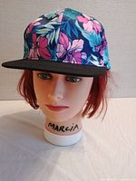 Front view of bright tropical floral snapback hat with black brim on mannequin head.